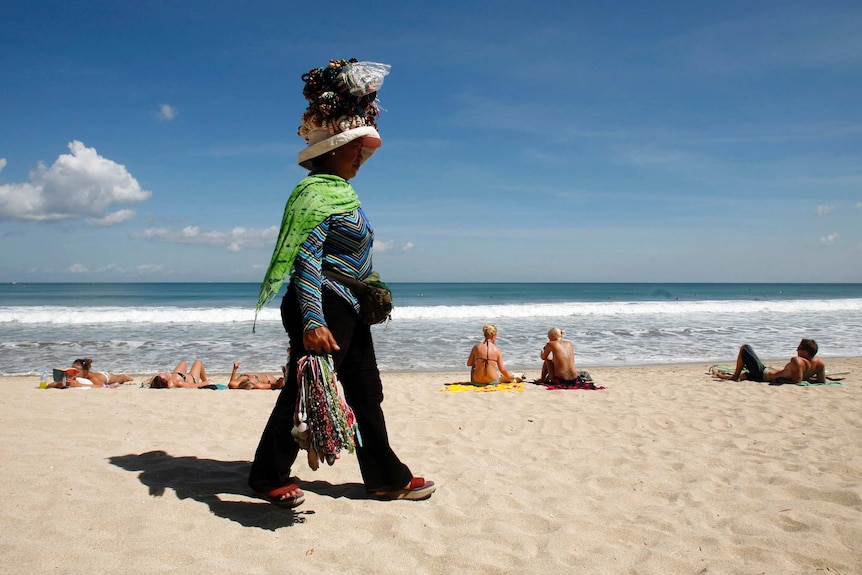 A souvenir seller walks along Kuta Beach, Bali.